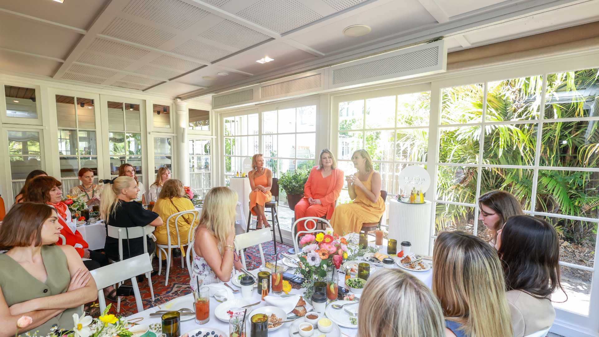 Group of people dining at a bright, window-lined room with a floral centerpiece.