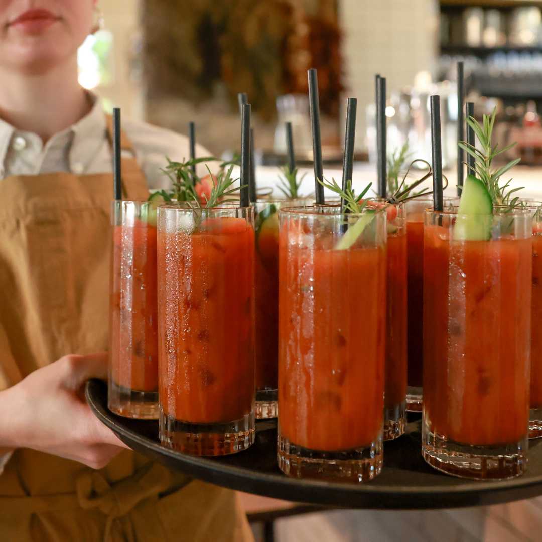 Waiter holding a tray of Bloody Mary cocktails garnished with rosemary.