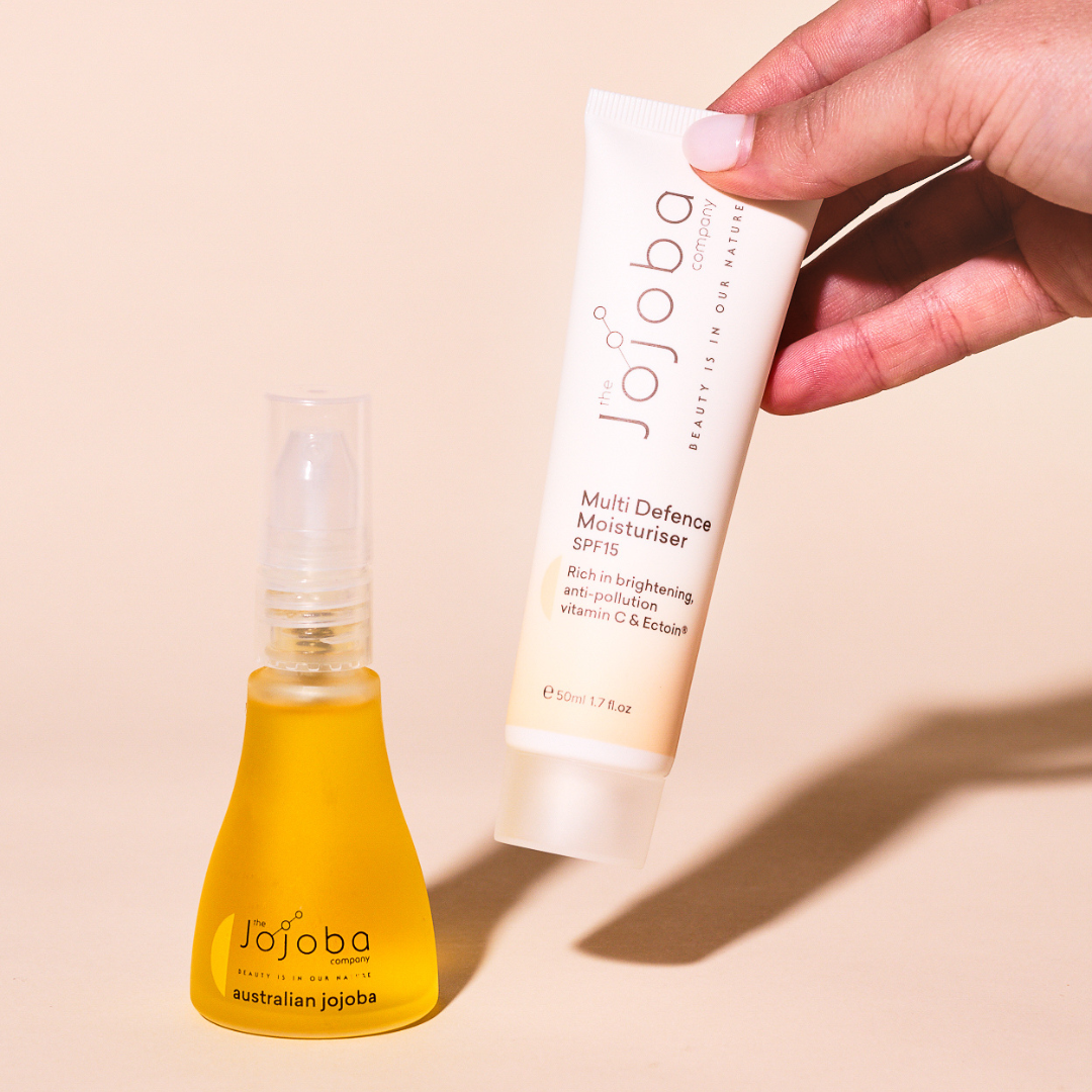 A hand holding a tube of Jojoba skin moisturizer next to a bottle of oil.