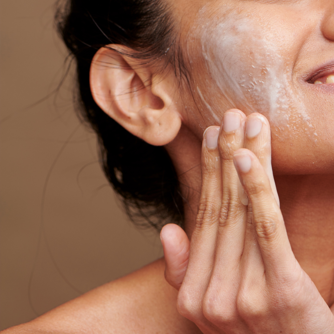 A woman is shaving her face with a scrub on her face.