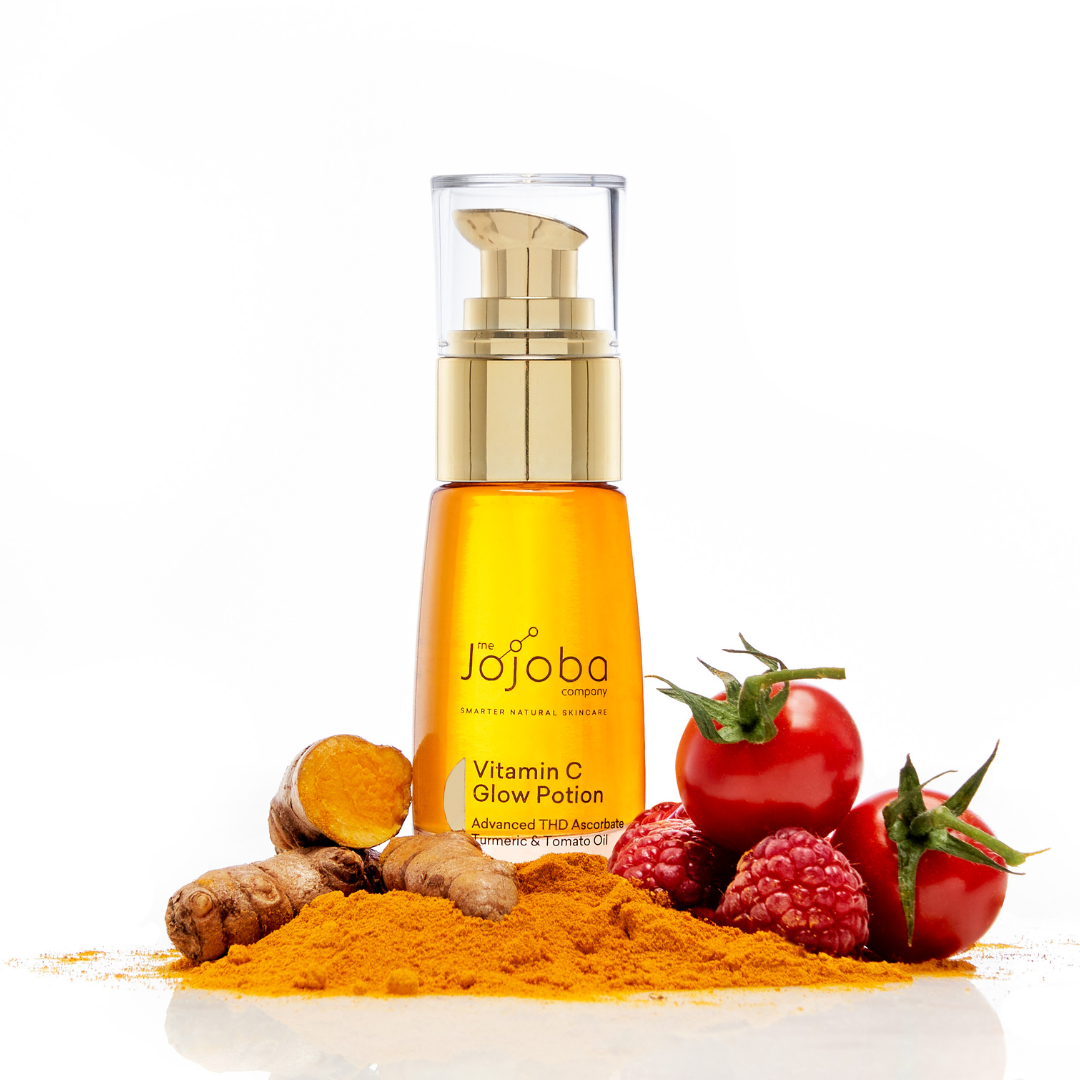 Skincare bottle with turmeric, tomatoes, and raspberries on white background.