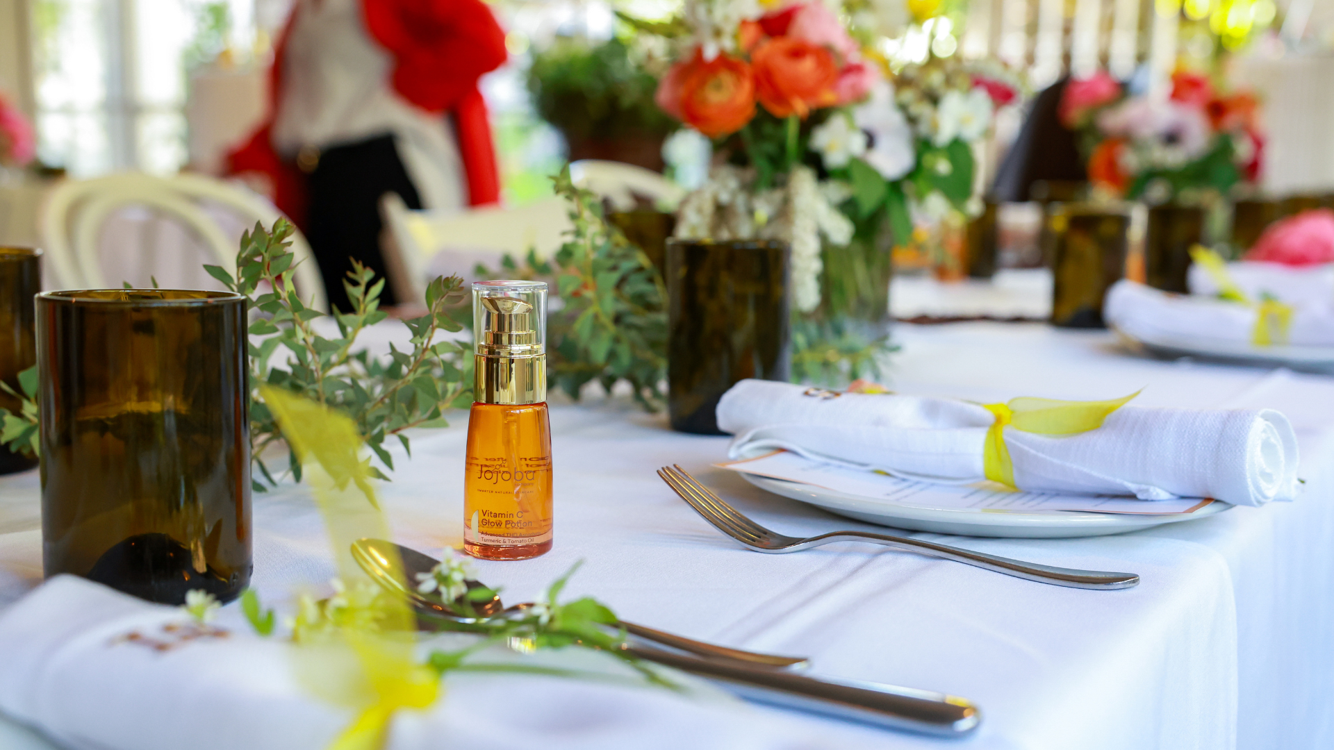 Elegantly set dining table with flowers, glassware, and a small bottle of jojoba oil.