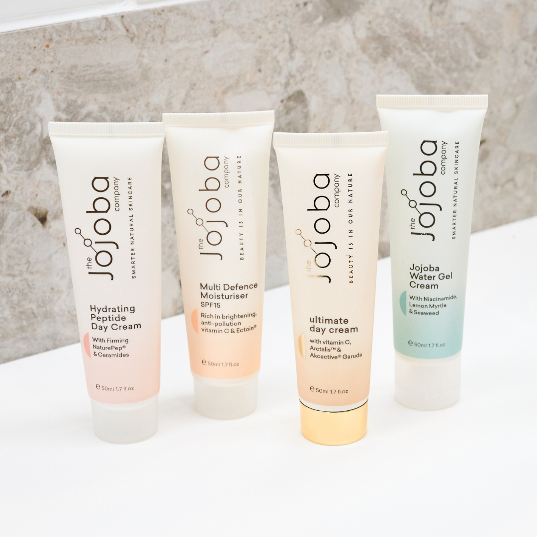 Four tubes of Jojoba skincare creams aligned against a marble background.