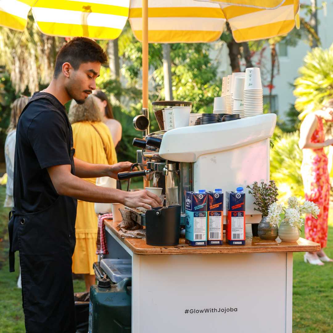 Barista working at an outdoor coffee cart with striped umbrella.