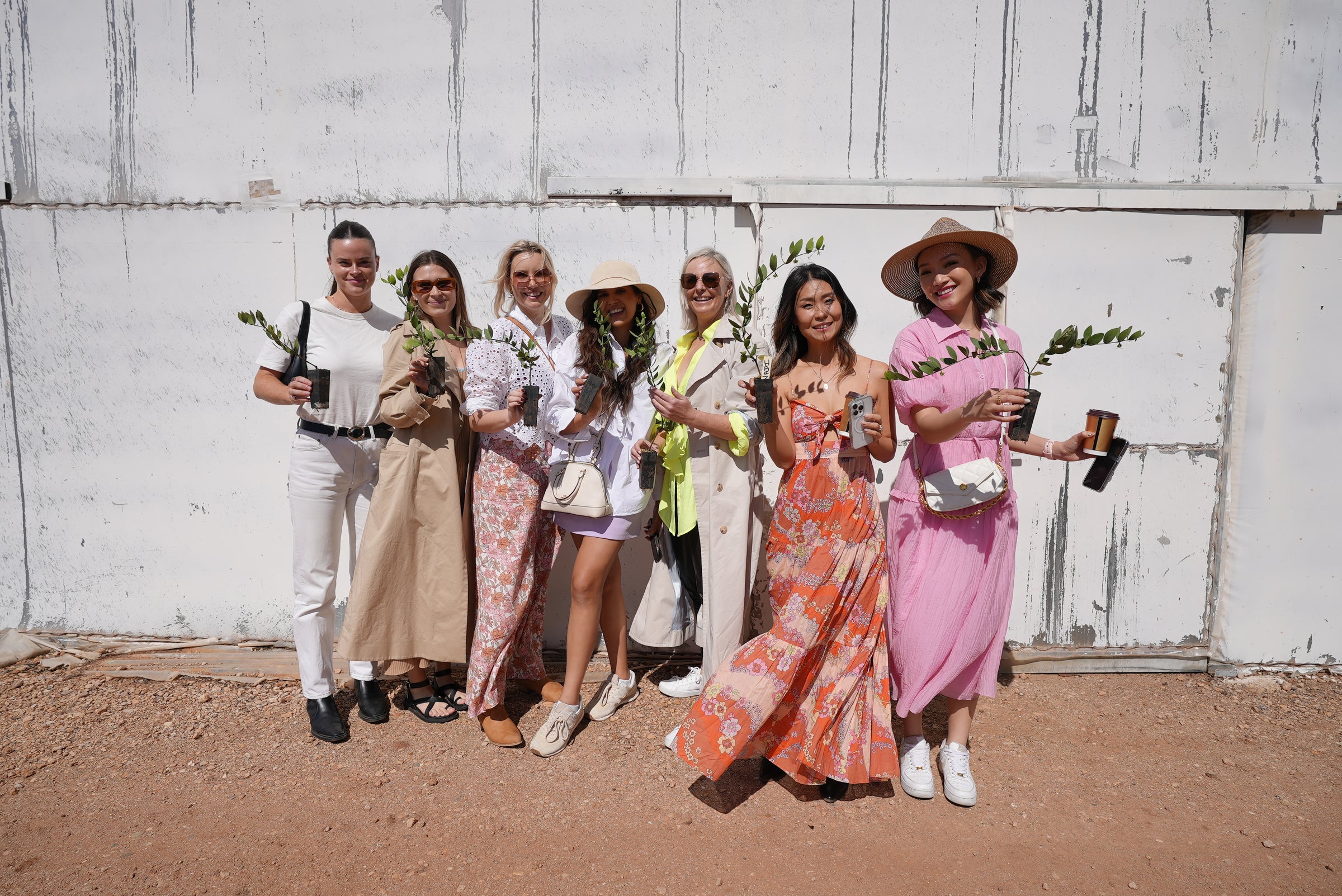 Women in elegant dresses and hats hold vibrant flowers in a sunny setting.