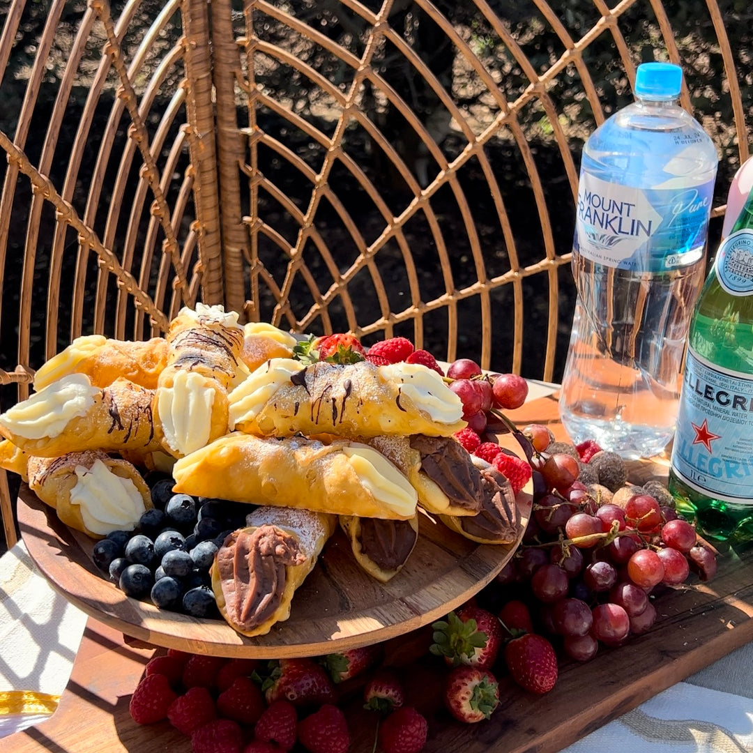 Picnic setting with cannoli, mixed berries, and bottled water on a wooden tray.