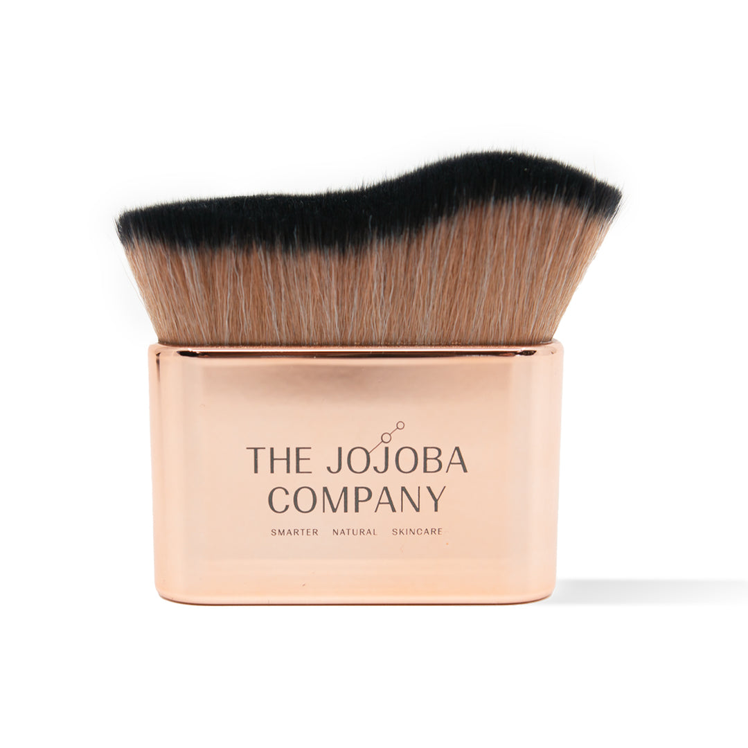 A flat-topped makeup brush with a rose gold handle labeled "THE JOJOBA COMPANY."