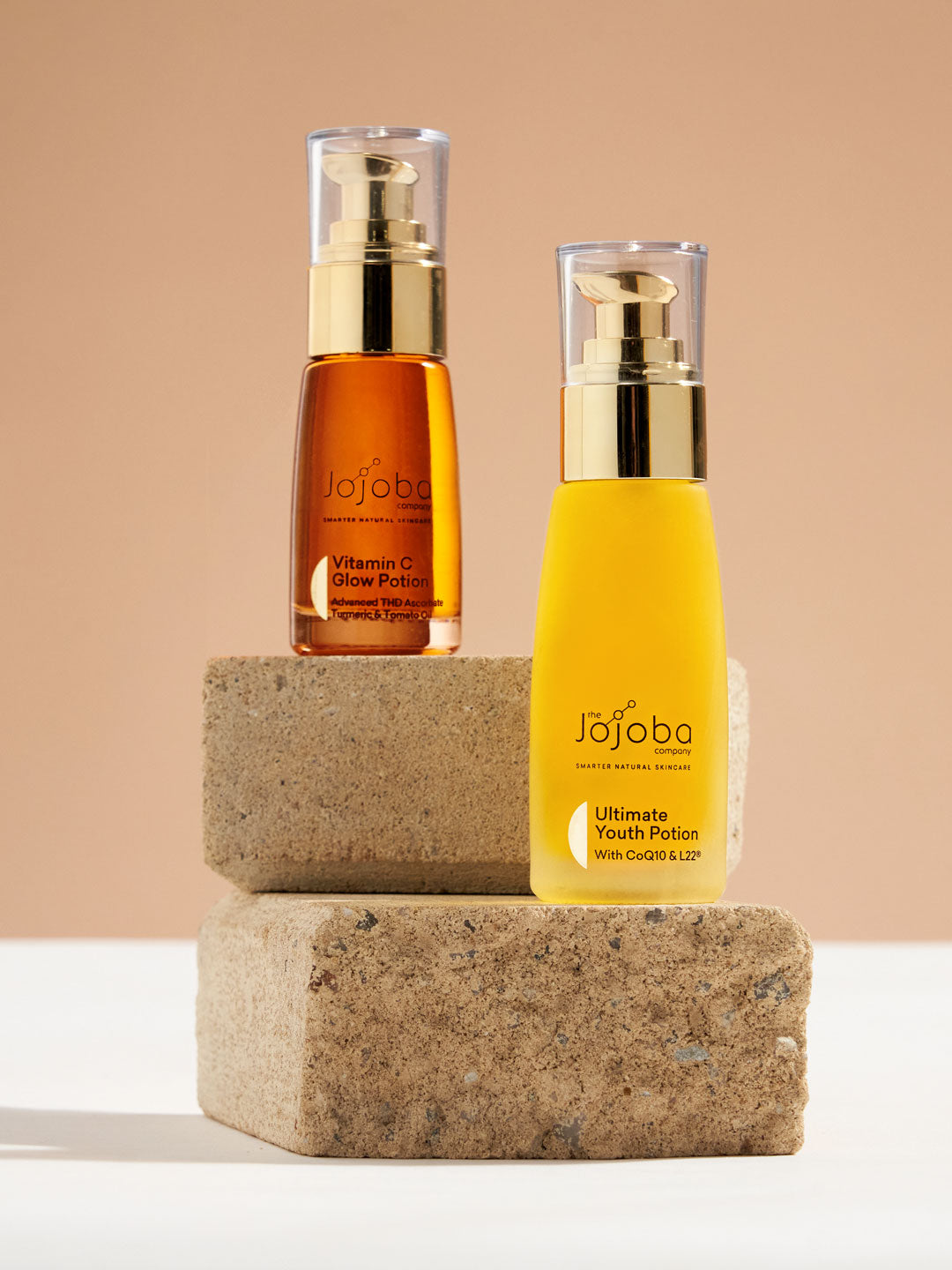 Two skincare serum bottles on cork stands against a peach background.